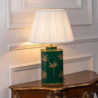 White shade table lamp with deep green ceramic base detailed with gold palm design ideal for luxury bedside or living room decor.