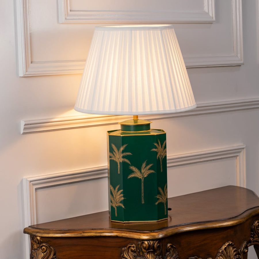 White shade table lamp with deep green ceramic base detailed with gold palm design ideal for luxury bedside or living room decor.
