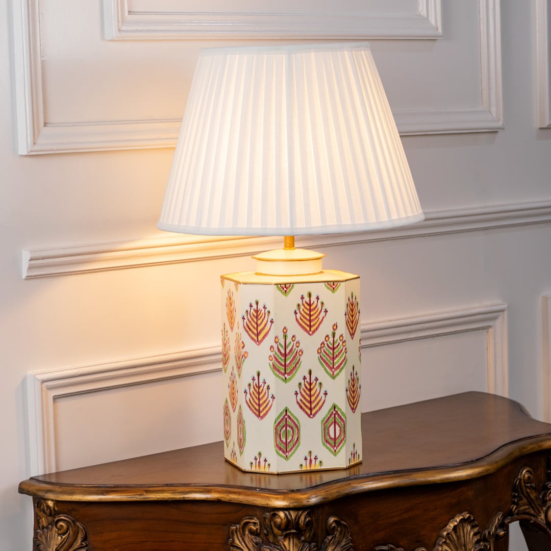 Table lamp on white background showcasing patterned ceramic base with intricate motifs and pleated shade creating elegant ambient glow.