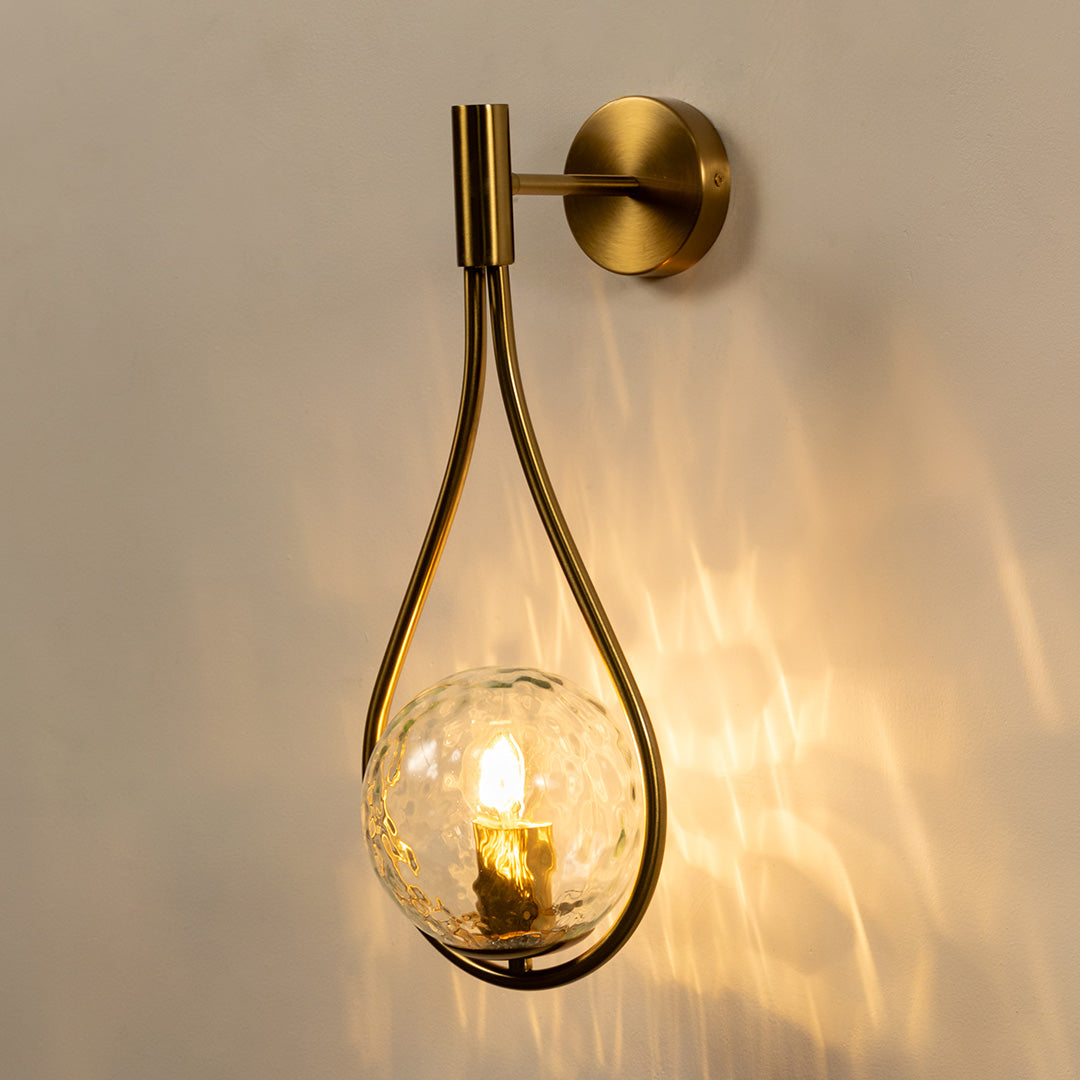 Modern gold metal wall light with clear glass globe for stylish bedroom and luxury decor styling spaces.

