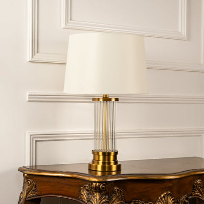 White shade gold rod base table lamp on carved console table with light off and white panel wall for elegant modern décor.