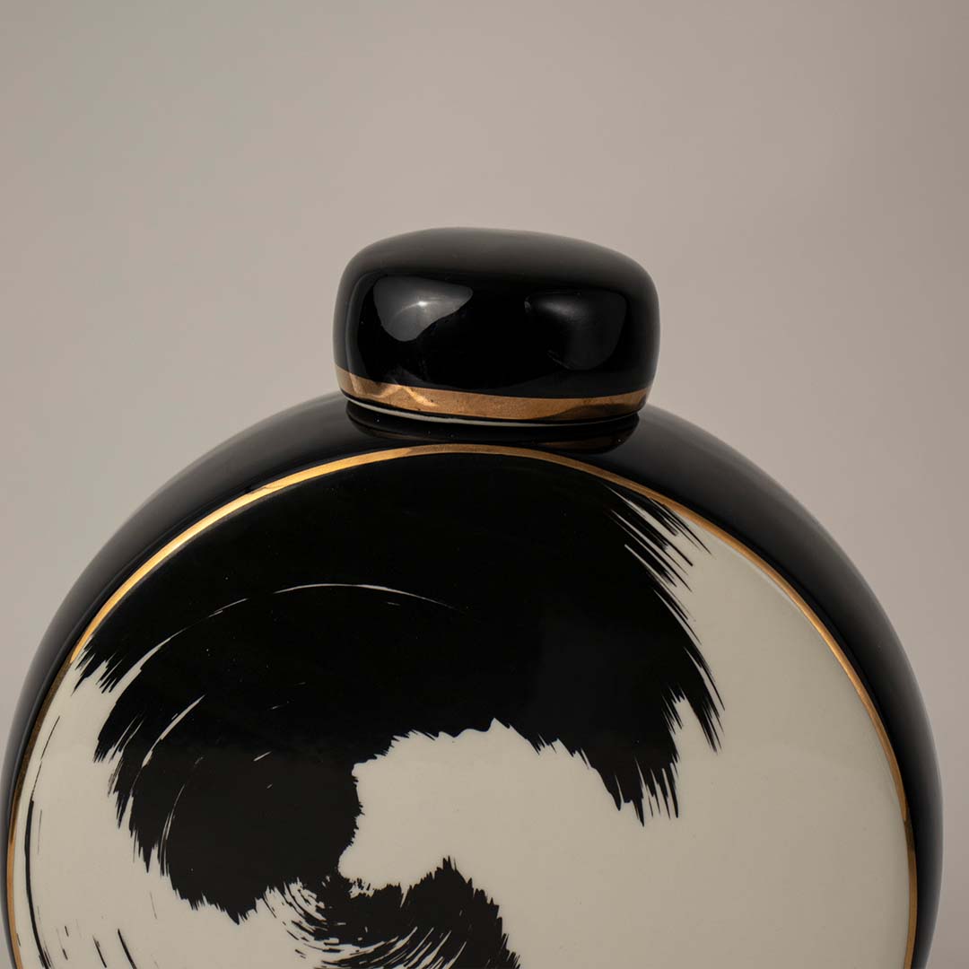 Glossy black ceramic vase with rounded body and small top opening placed on white surface against neutral background closeup highlighting reflective modern decor appeal.