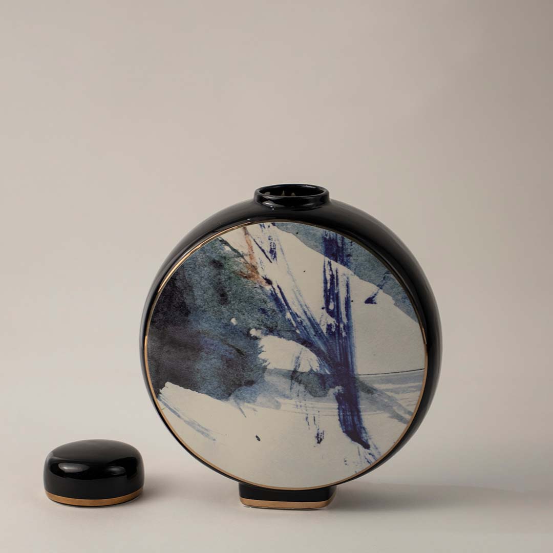 Round black ceramic vase with blue and white abstract brush art placed on white background for modern home decor.