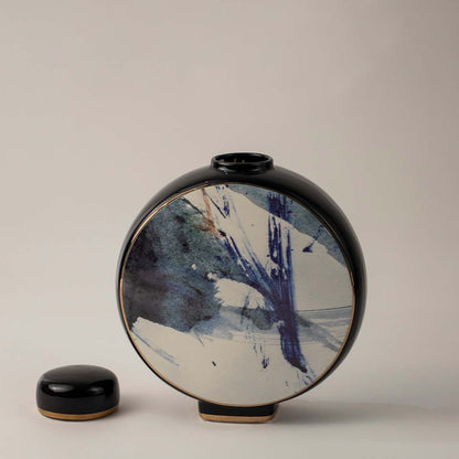 Round black ceramic vase with blue and white abstract brush art placed on white background for modern home decor.