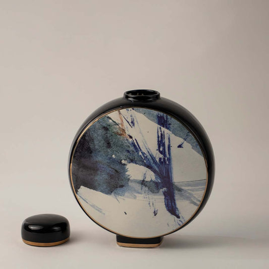 Round black ceramic vase with blue and white abstract brush art placed on white background for modern home decor.