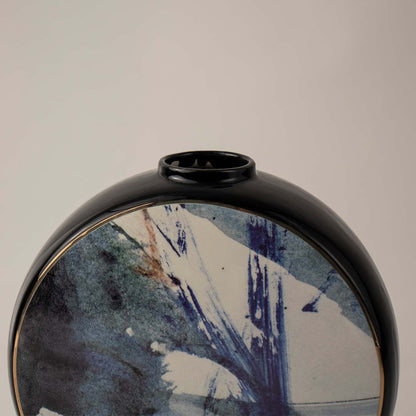 Round ceramic vase with artistic blue brushstroke design and black rim placed on white surface against neutral background showcasing modern abstract home decor styling.