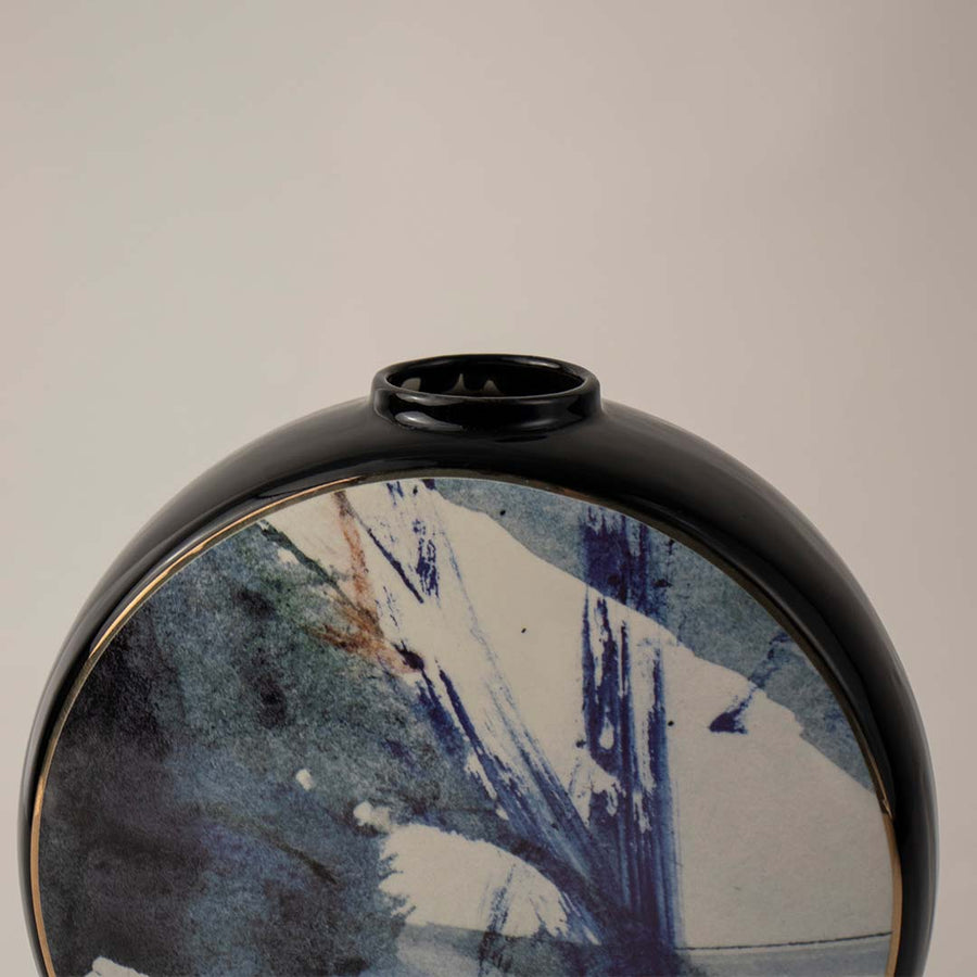 Round ceramic vase with artistic blue brushstroke design and black rim placed on white surface against neutral background showcasing modern abstract home decor styling.