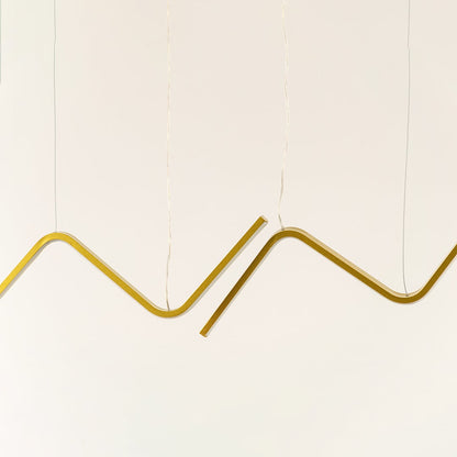 Gold sculptural chandelier featuring sweeping wave shaped LED bars suspended elegantly creating a warm dynamic decorative lighting accent in the modern room.