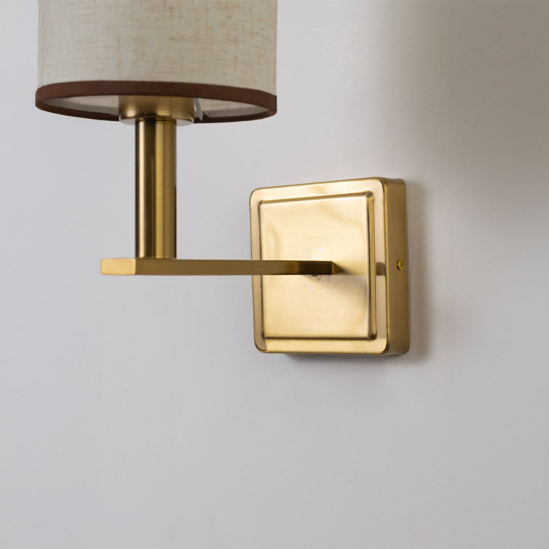 Closeup wall light in gold metal finish with fabric shade for bedroom or living room decor lighting white background.