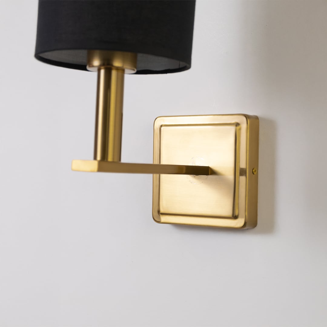 Closeup view of gold wall sconce with black drum shade showing fine metal detailing and modern lighting design.