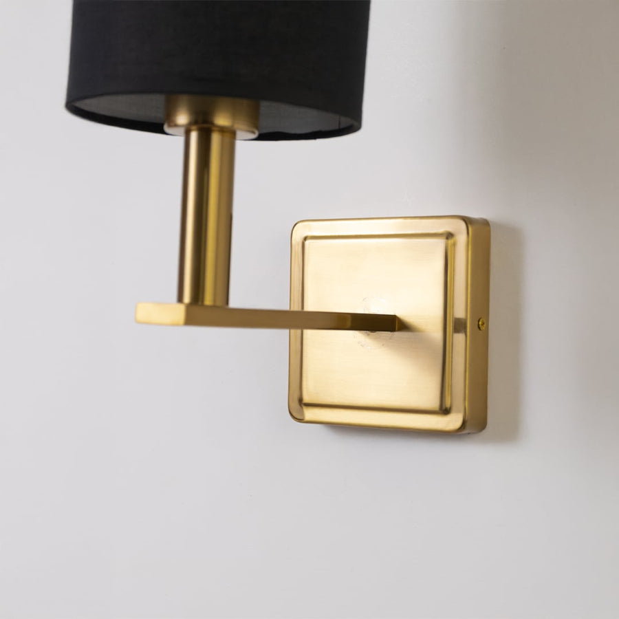 Closeup view of gold wall sconce with black drum shade showing fine metal detailing and modern lighting design.