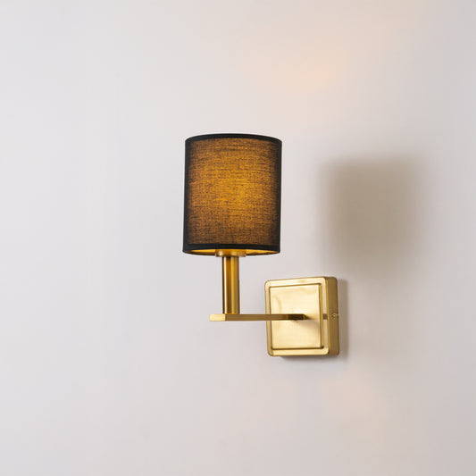 Contemporary wall light in gold metal finish with dark fabric shade for bedroom or living decor lighting white background.