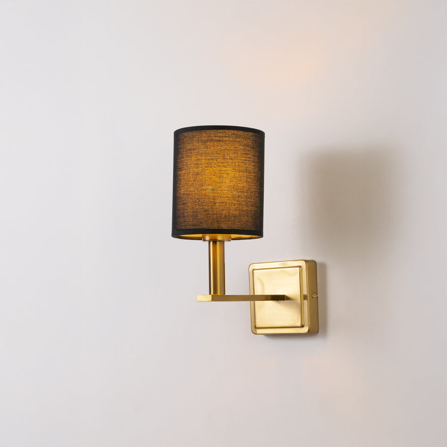 Contemporary wall light in gold metal finish with dark fabric shade for bedroom or living decor lighting white background.
