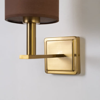 Closeup view of gold wall sconce with brown drum shade showing detailed metal finish and modern lighting design.