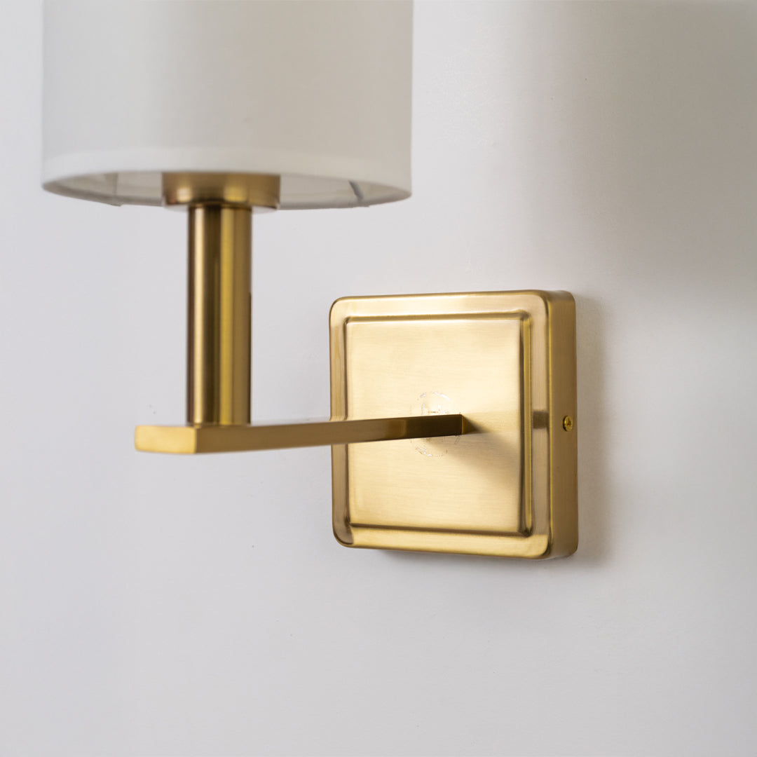 Closeup wall light in gold metal finish with fabric shade for bedroom or living room decor lighting white background.