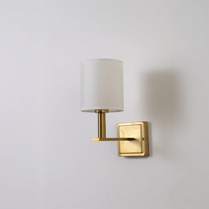 Gold wall sconce with white drum shade shown switched off on white background for clean minimal stylish wall decor.