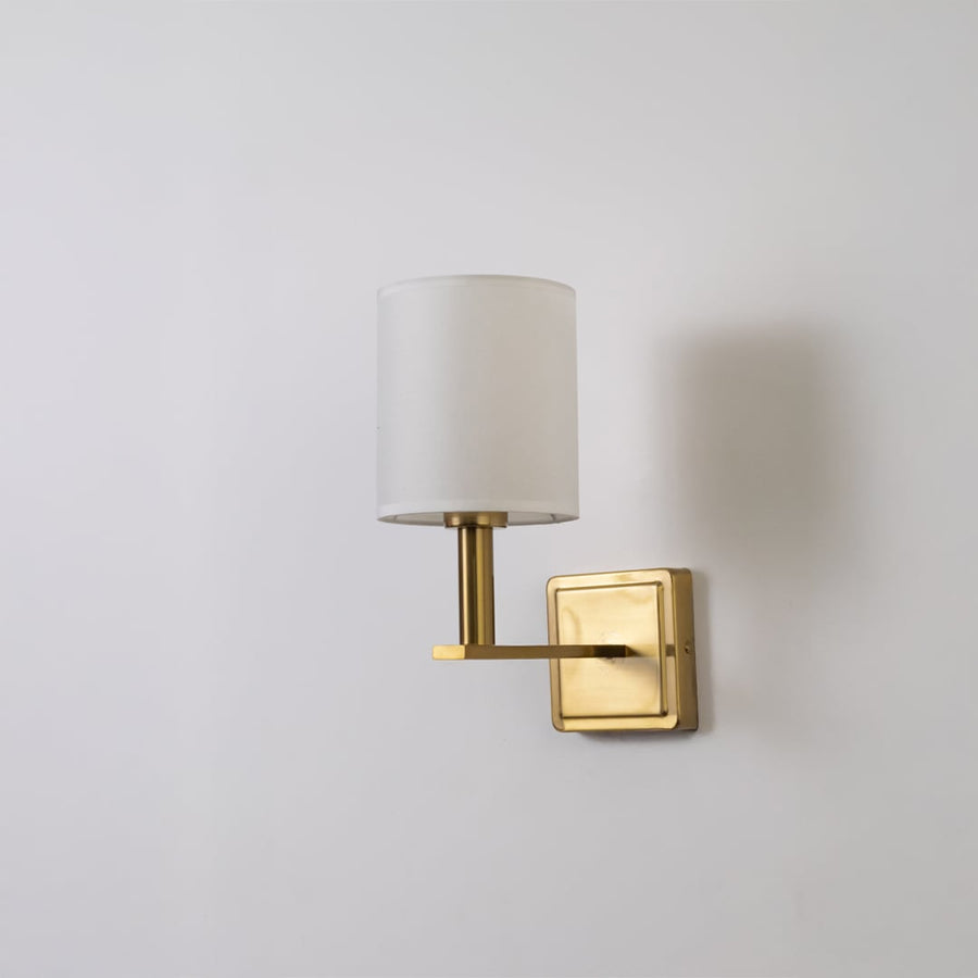 Gold wall sconce with white drum shade shown switched off on white background for clean minimal stylish wall decor.