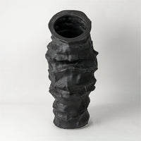 Black ceramic vase with stacked textured ring design placed on white surface against neutral background showcasing bold sculptural modern decor styling.