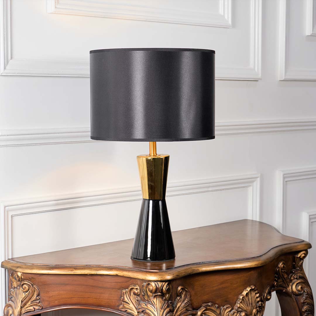 Black fabric shade table lamp with gold metal stem and dark ceramic base for modern luxury interior decor.