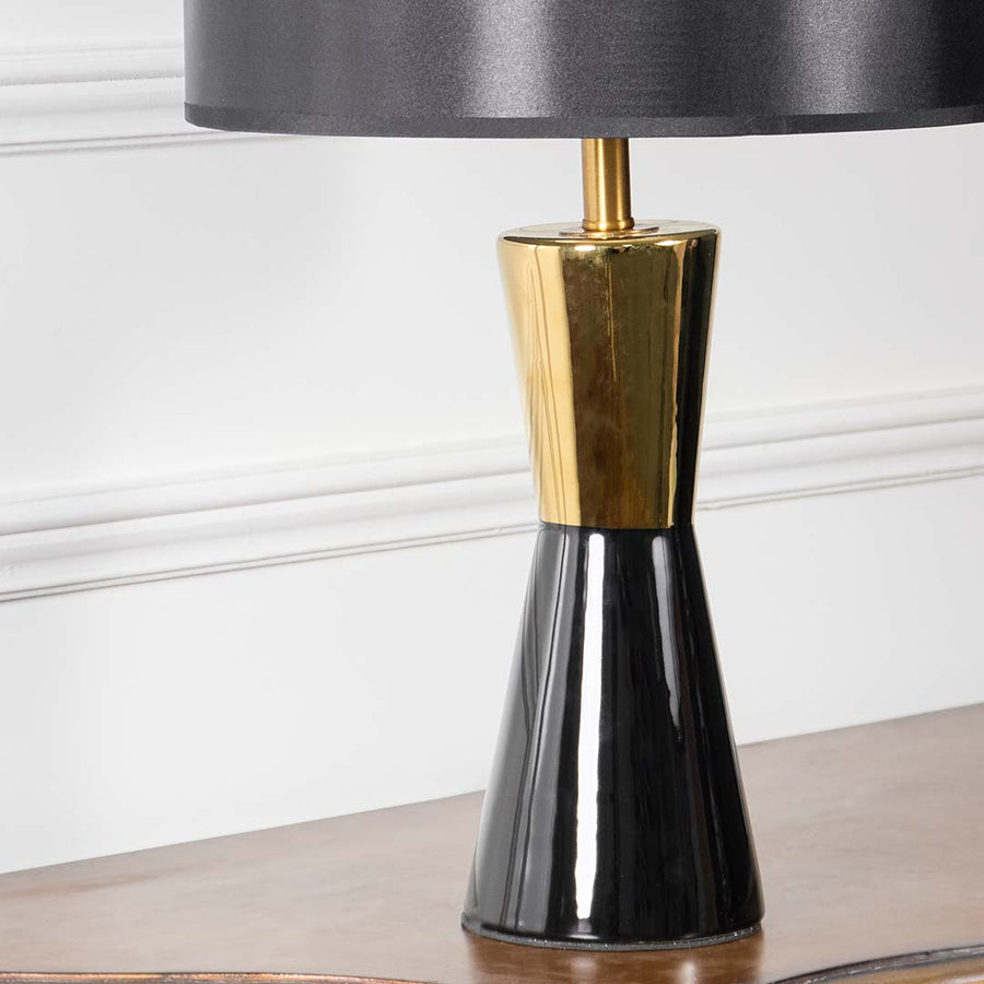 Closeup of modern table lamp showing black and gold two-tone ceramic base detail with black fabric drum shade styling.