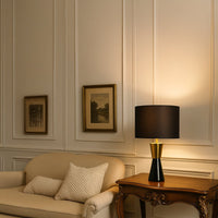 Black and gold table lamp with drum shade displayed on vintage console creating elegant modern classic interior lighting.