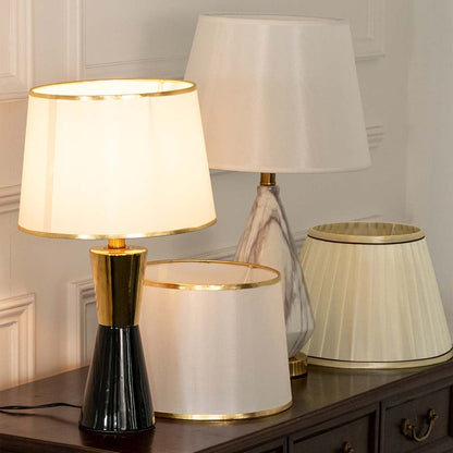 White pleated shade black and gold table lamp on wooden sideboard with light off for chic modern décor.