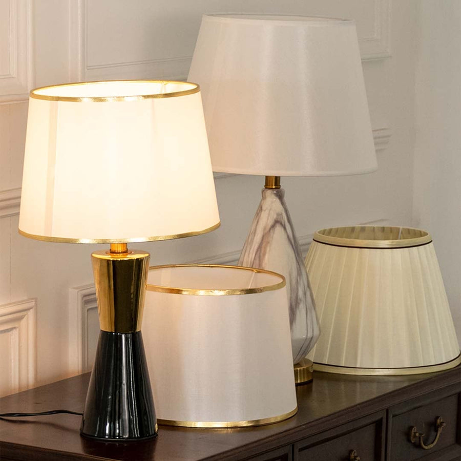 White pleated shade black and gold table lamp on wooden sideboard with light off for chic modern décor.