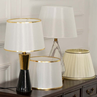 White pleated shade black and gold table lamp on wooden sideboard with light off for chic stylish modern décor.