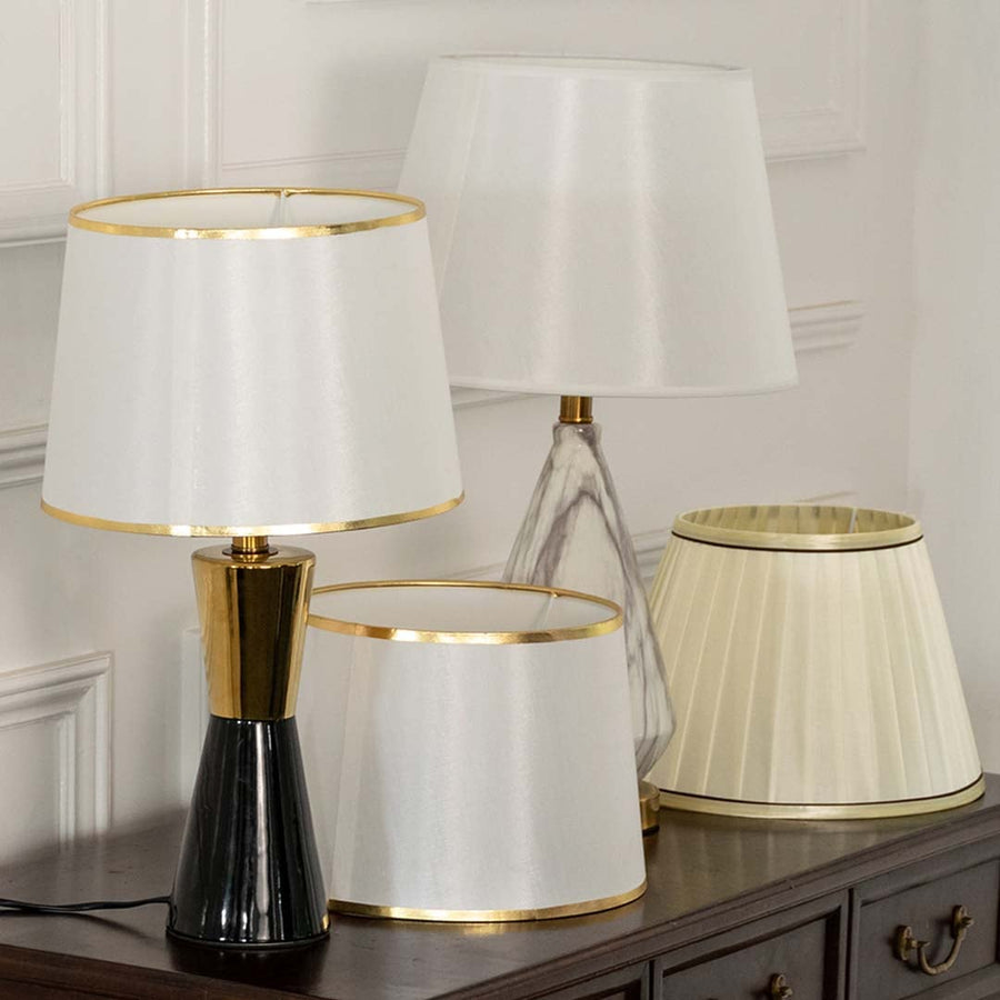White pleated shade black and gold table lamp on wooden sideboard with light off for chic stylish modern décor.