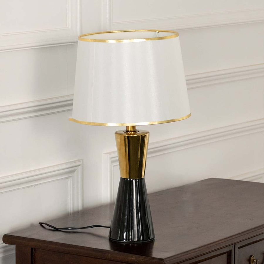 White pleated shade black and gold table lamp on wooden sideboard with light off for chic modern décor.