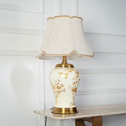 Table lamp with cream ceramic base and gold floral design displayed on a white background for clear product viewing.