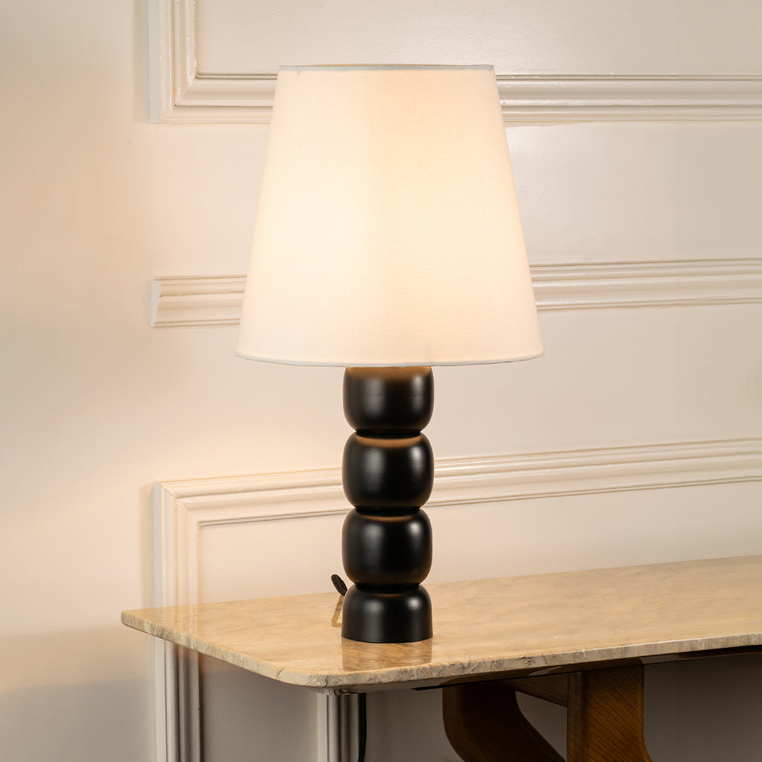 Table lamp with white fabric shade and black sculpted base ideal for bedroom or living room table decor styling on clean background.