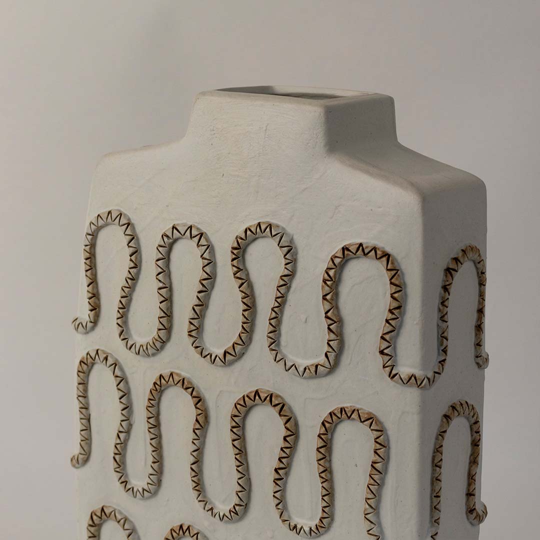 White ceramic vase with embossed loop pattern and matte finish placed on white surface against neutral background showcasing contemporary artistic home decor styling.
