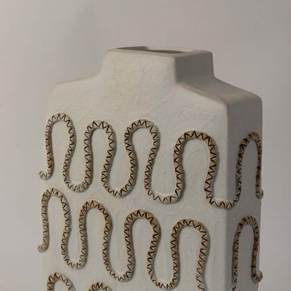 White ceramic vase with embossed loop pattern and matte finish placed on white surface against neutral background showcasing contemporary artistic home decor styling.