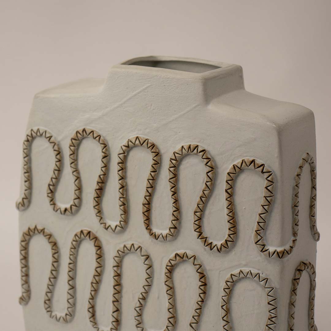 Decorative white ceramic vase with textured loop design placed on white surface against neutral background enhancing modern sculptural home decor appeal.