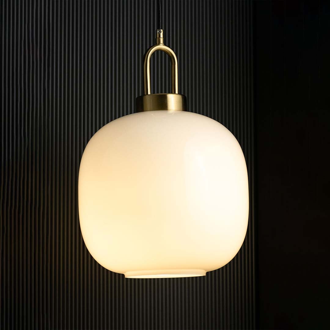A gold and white pendant light with lights on casting a warm glow on a dark backdrop showcasing its rounded white glass shade and gold fitting.