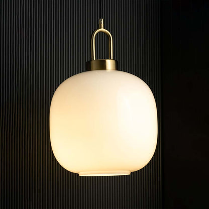 A gold and white pendant light with lights on casting a warm glow on a dark backdrop showcasing its rounded white glass shade and gold fitting.