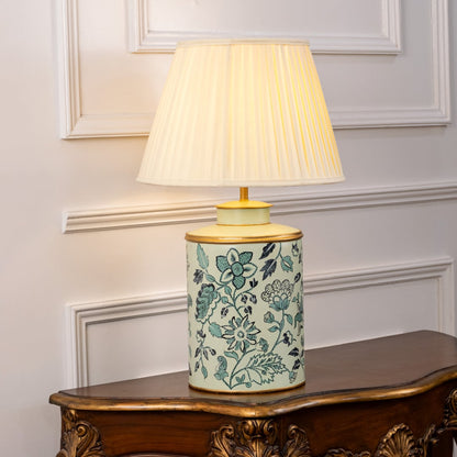 Table lamp on white background featuring teal floral ceramic base paired with a pleated fabric lampshade glowing softly.