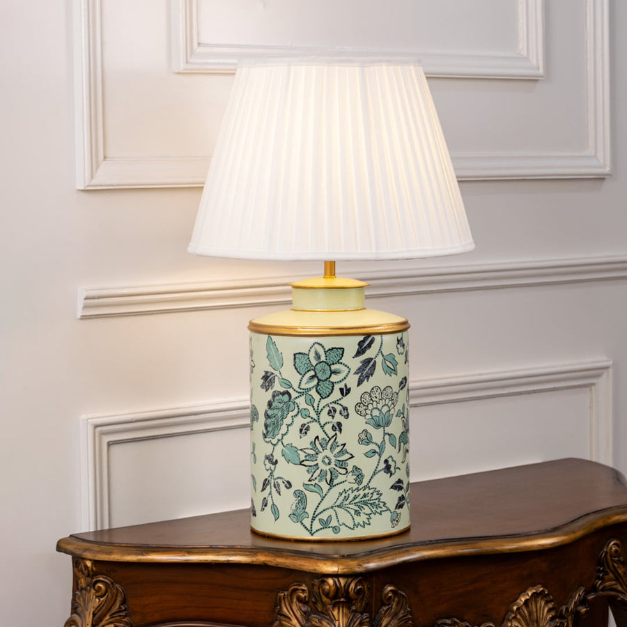 Table lamp showcasing a green floral ceramic base with a pleated lampshade placed against a white background.