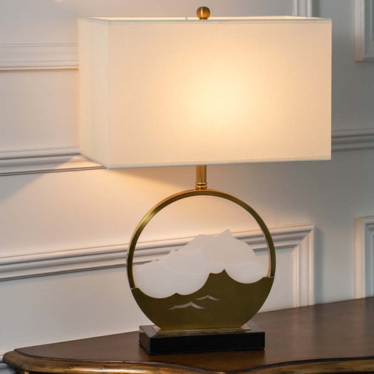 Green glass table lamp with fabric drum shade and gold ring base creating elegant modern ambient lighting indoors.