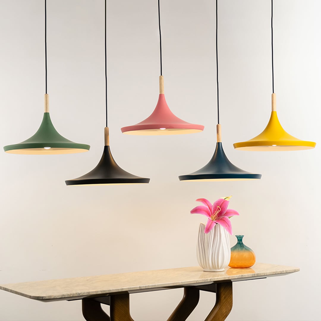Colorful pendant lights in yellow black green pink and blue with wooden accents hanging above a dining table with flowers.