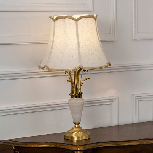 Gold and white marble base table lamp with cream fabric shade turned on against white background bedside table lamp.