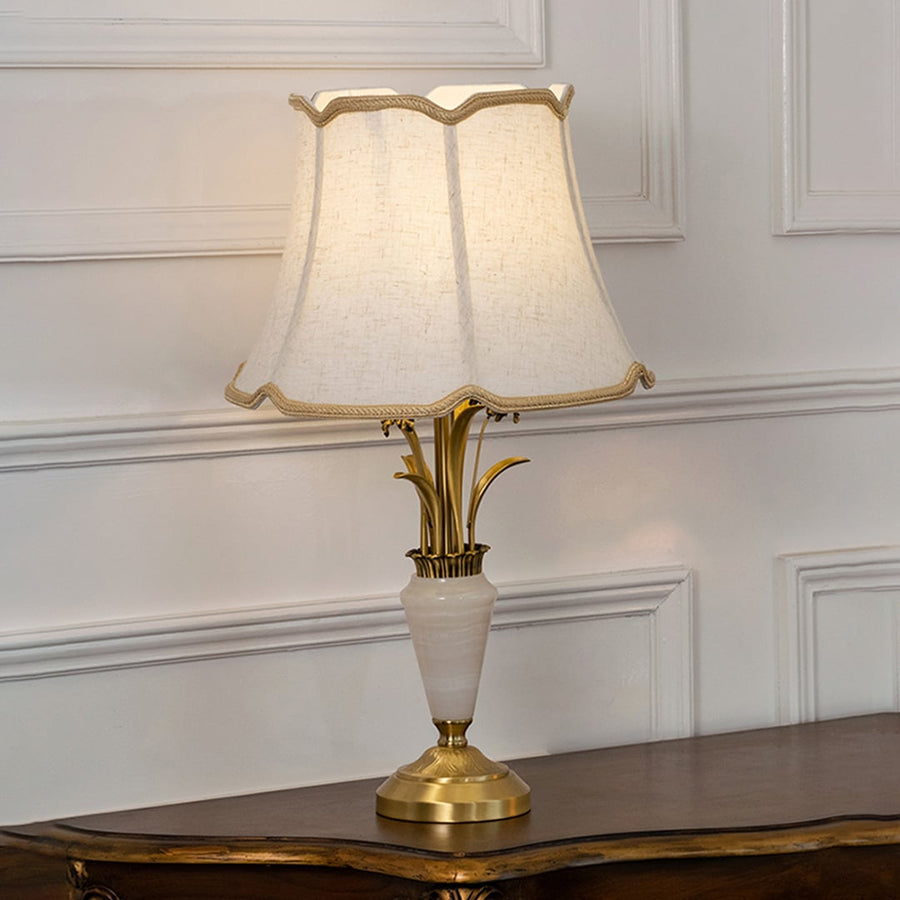 Gold and white marble base table lamp with cream fabric shade turned on against white background bedside table lamp.