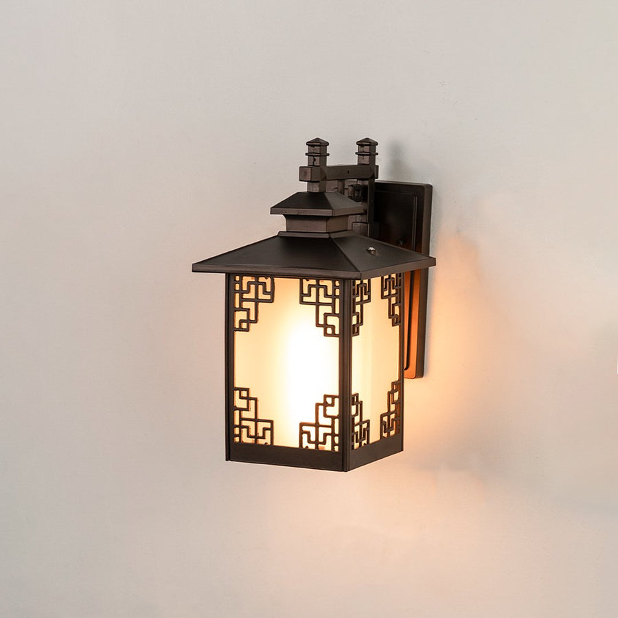 Black metal outdoor wall lantern on white background with Greek key corner lattice frame design and frosted glass panels.