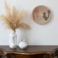 Handwoven wall basket decor in natural pink and black fiber styled above wooden console table for boho wall.