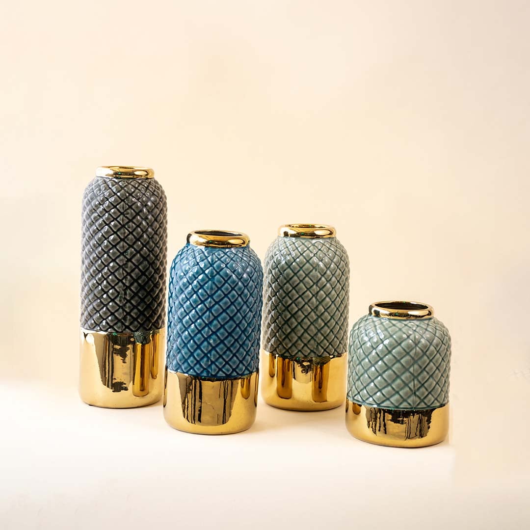 A collection of textured ceramic vases in grey blue and teal tones with glossy gold bases displayed together on a white background showcasing coordinated decor styling.