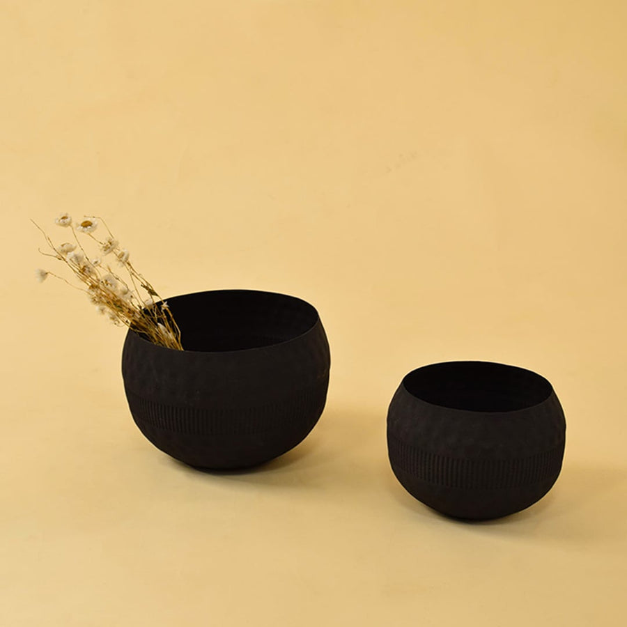 Black textured planter bowl with matte finish displayed with other decor pieces in a warm minimal lifestyle setting.
