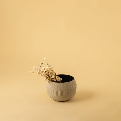 Small cream round textured pot with matte black interior styled in a warm modern home setting adding natural minimal decor charm.