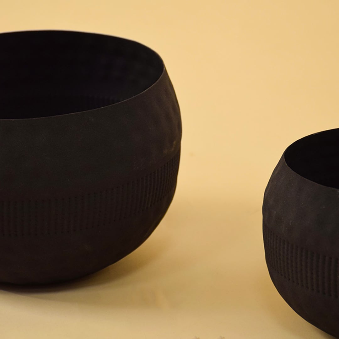 Closeup of black textured planter bowl shown alongside other pieces highlighting its handcrafted details and matte finish.
