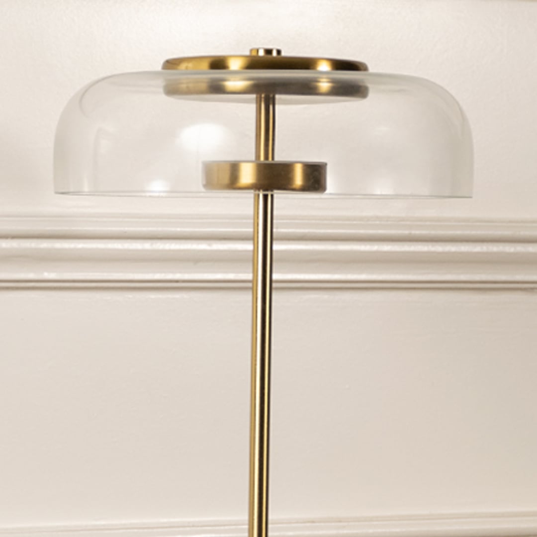 Closeup of gold and clear glass dome table lamp highlighting its polished metal finish sleek stem and smooth transparent shade.